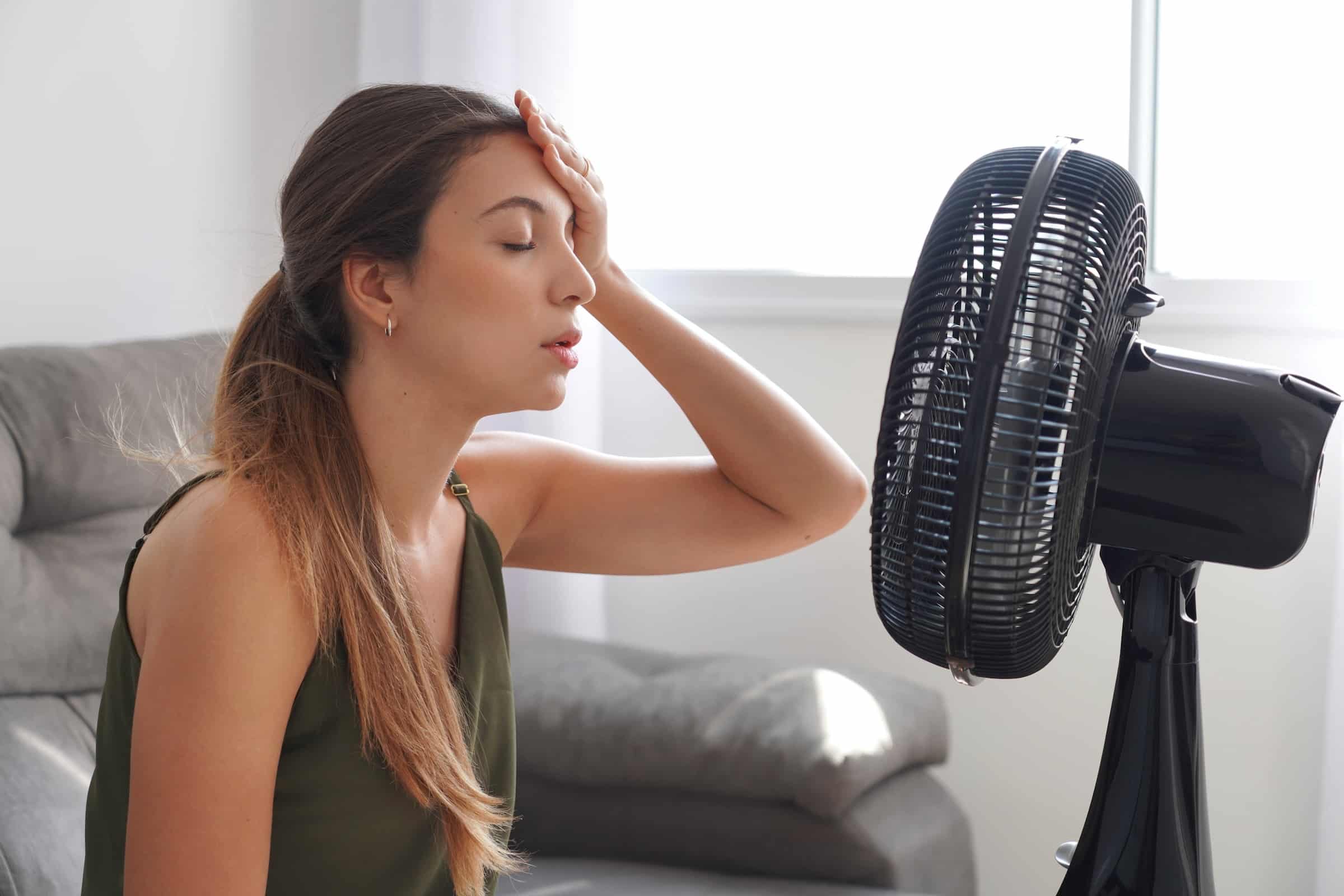 Woman overheating and trying to cool down in front of fan in house
